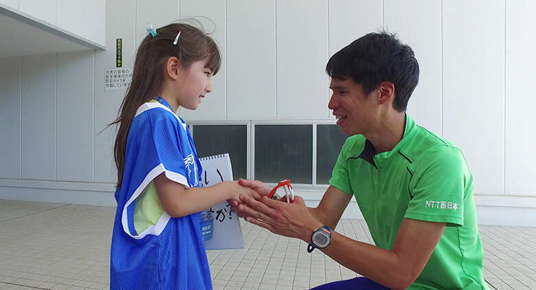 Image: Photograph of a little girl Kids' Reporter nervously shaking Tadashi Horikoshi's hand, who is crouched down to her eye-level and smiling.