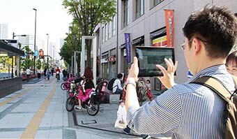 Image: Photograph from behind of a male survey team member using a tablet to take and record photographs of the streetscape.