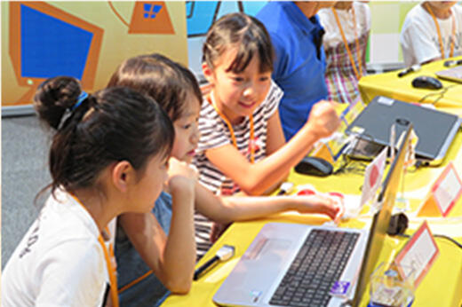 ノートパソコンを前に相談しながら検索をしている子どもたち